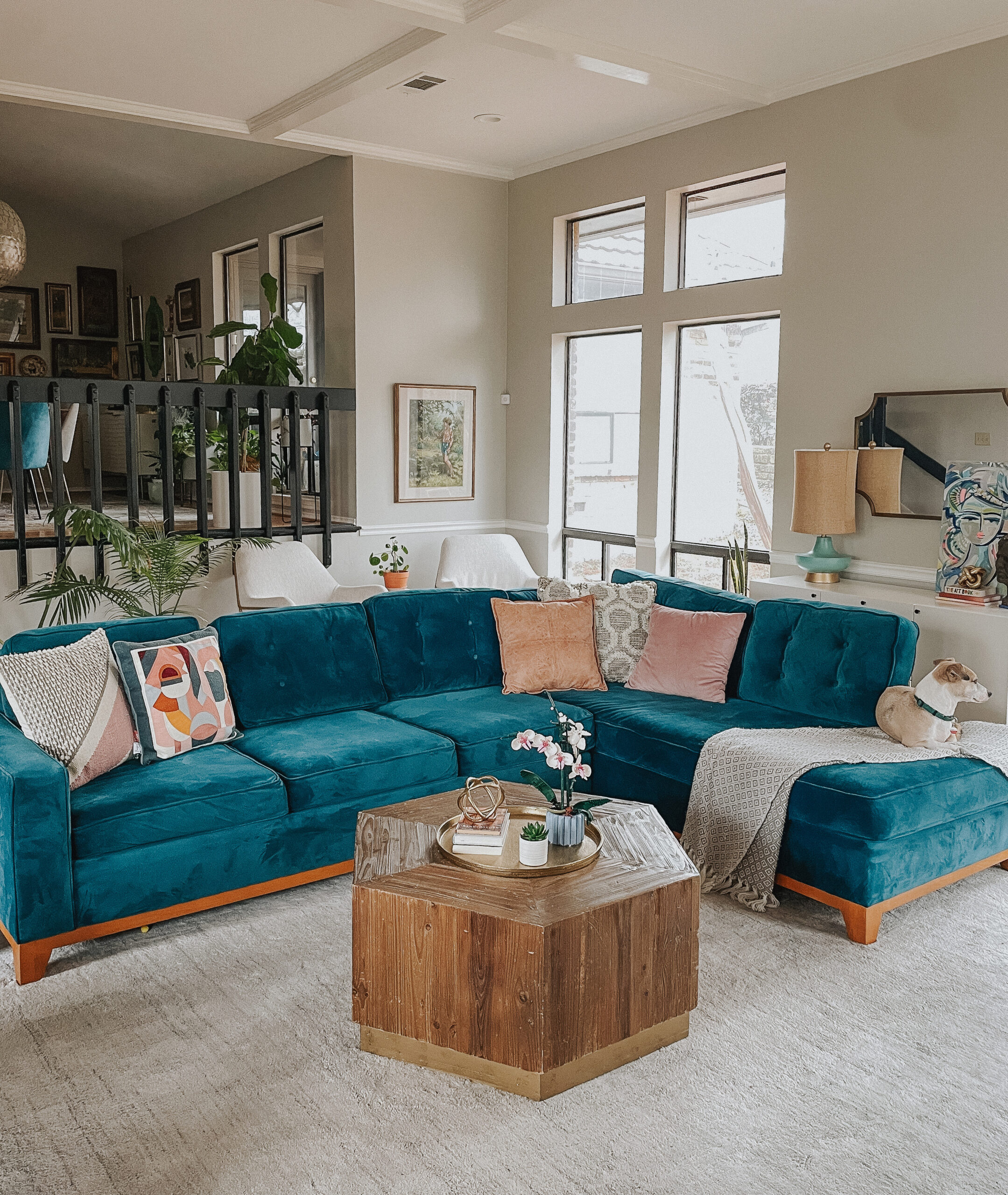 modern living room with bold teal sectional and colorful pillows and floor to ceiling windows