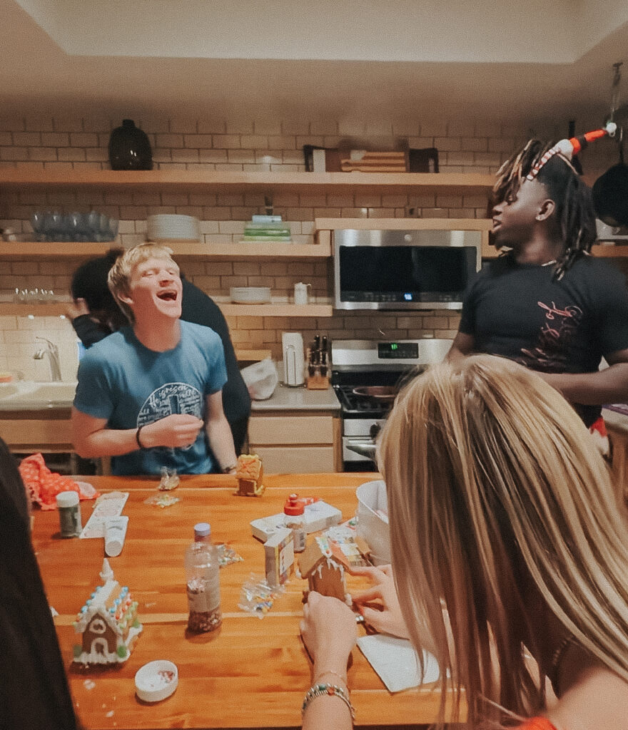 Family and friends gathered around the table making memories at a holiday gingerbread house party