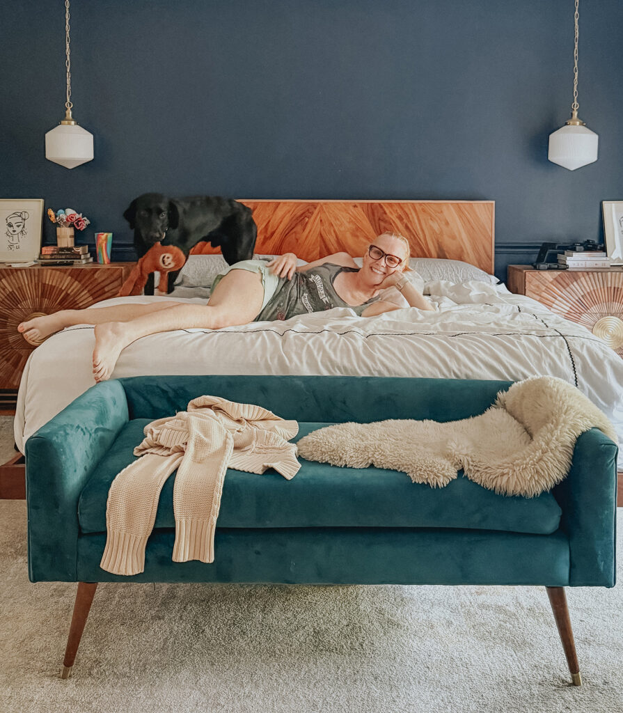 bedroom with navy wall, a teal bench, a black lab and a messy bed