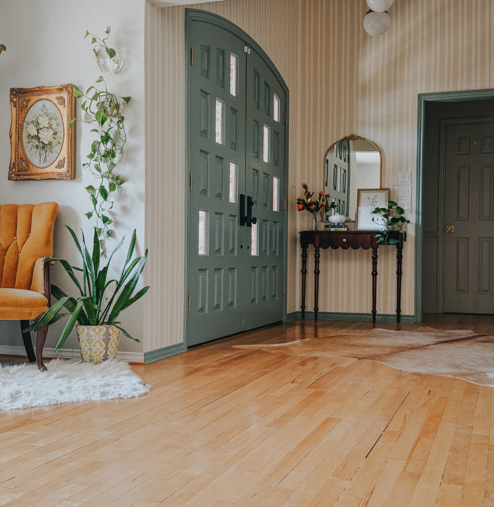 Updated entryway with subtle striped wallpaper, vintage furniture, and collected home decor