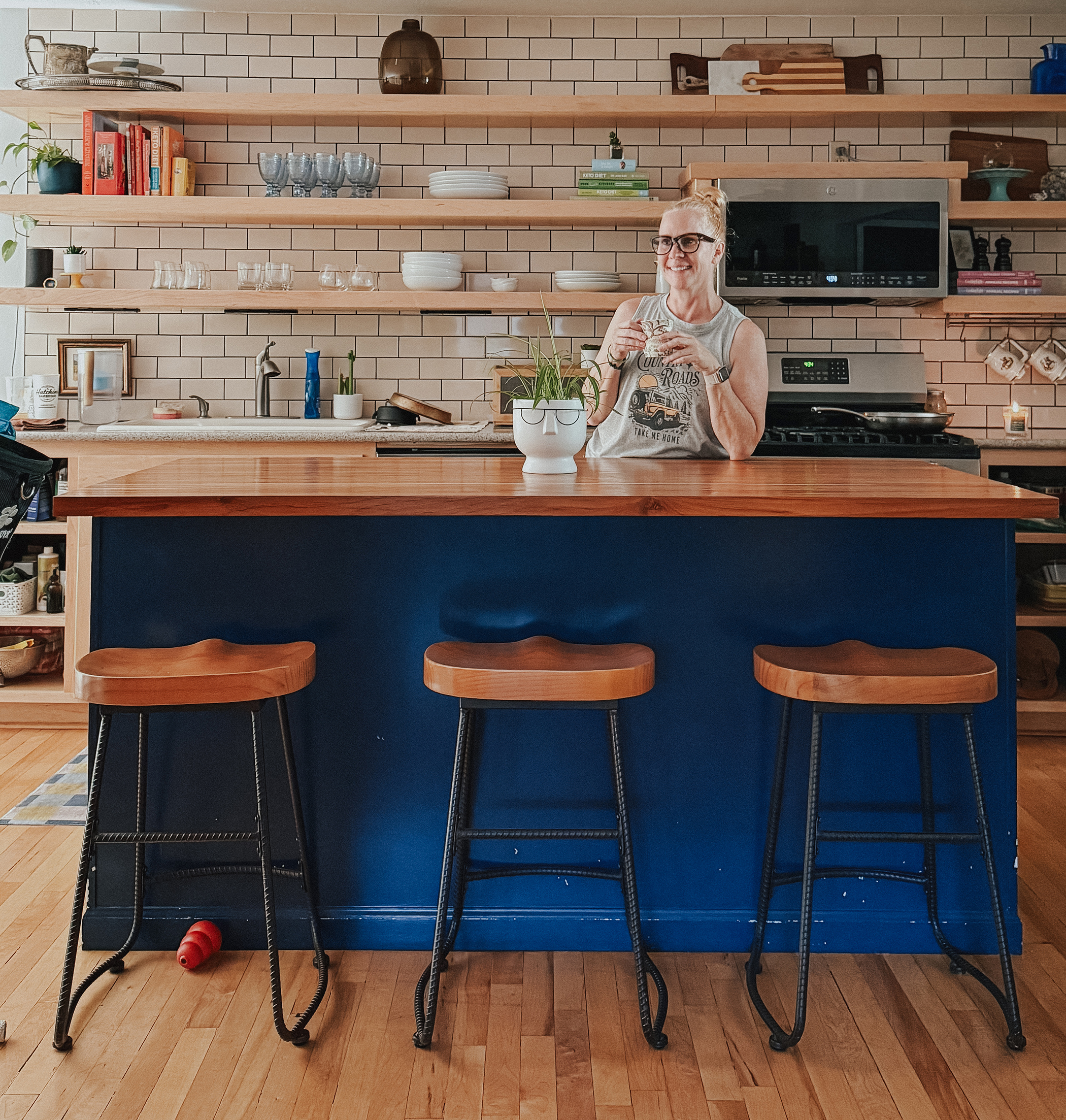 Redhead standing in her kitchen with open shelving and a navy island with wooden barstools